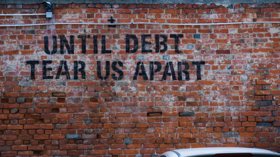 A brick wall with the text "Until debt tear us apart". Photo.