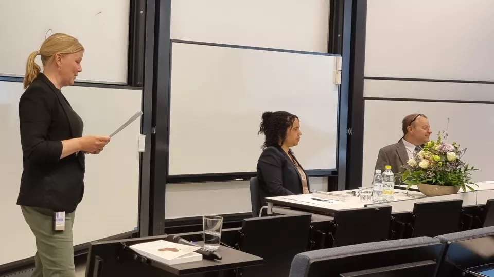 Three persons in a lecture hall during dissertation, main supervisor holding a paper and talking to defendent and opponent. Photo: Björn Frostner