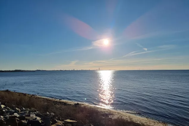 Sun reflecting in ocean with rocky beach. Photo.