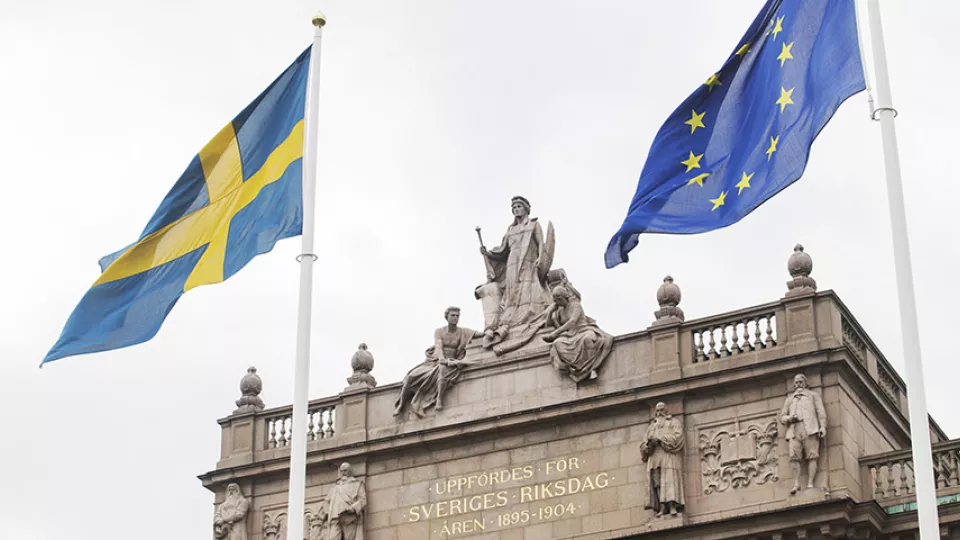 En svensk flagga och en EU-flagga framför riksdagshuset.