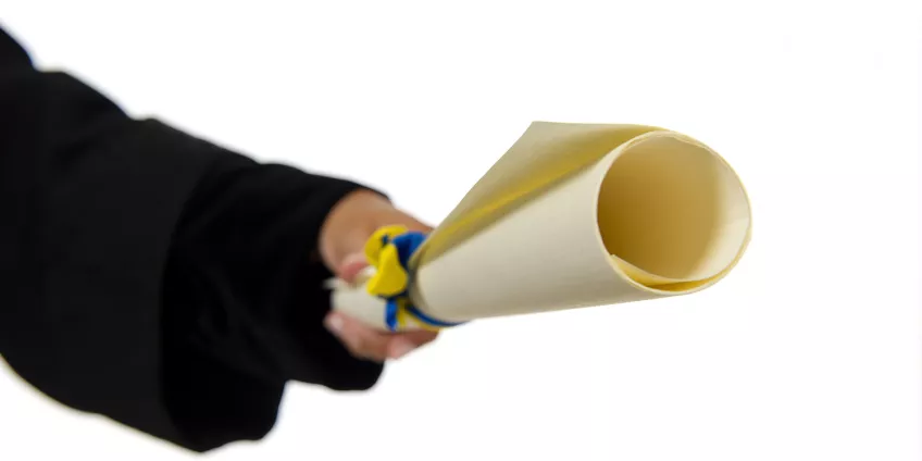 En hand håller fram ett examensdiplom. Foto.