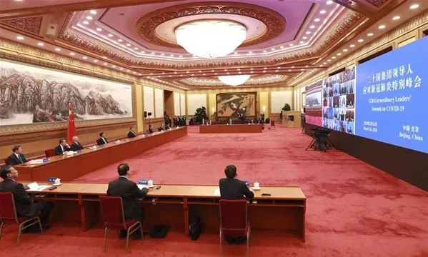 Kinas ledare Xi Jinping på ett videomöte i Folket stora hall i Peking. Runt honom sitter flera personer. Foto.